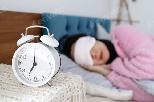 Preview: Sleepy young Asian woman in bed with eyes closed extending hand to alarm clock at home.