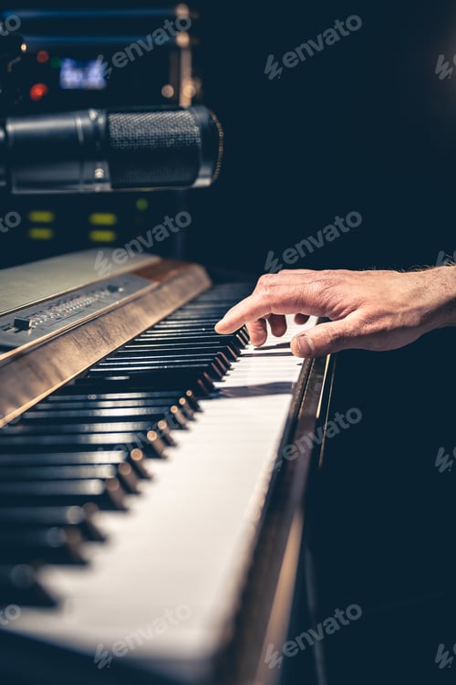 Preview: A man's hand plays the piano keys in a dark interior of a music studio.