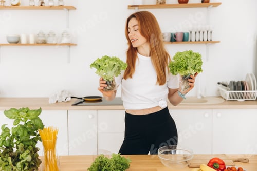 Preview: Mature sporty muscle woman in braces is holding some lettuce leaves in the home kitchen