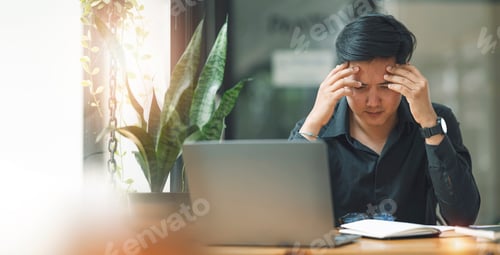 Preview: Stressed businessman with laptop computer sitting at casual office. hand on his head.