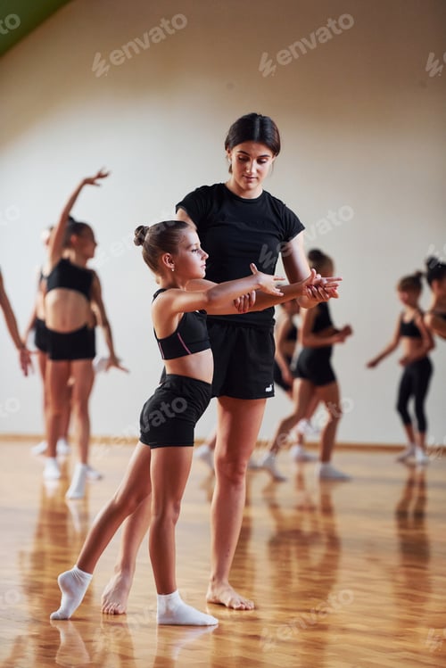 Preview: Woman teaching and helping. Group of female kids practicing athletic exercises together indoors
