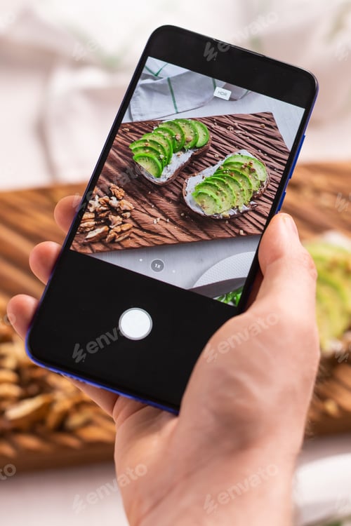 Preview: Hands take pictures on smartphone of two beautiful healthy sour cream and avocado sandwiches lying