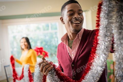 Preview: A young couple hanging tinsel up, decorating a house at Christmas.