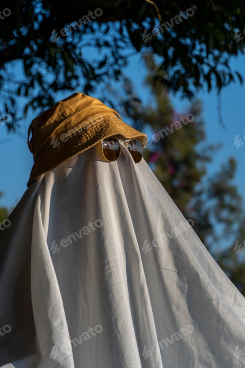 Preview: Person wearing a hat and black-rimmed sunglasses over a white cloth resembling a ghost