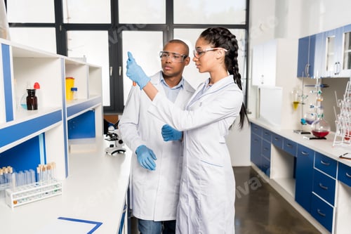 Preview: Young scientists in lab coats analyzing test tubes in laboratory and discussing