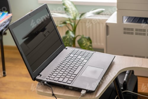 Preview: Open black laptop computer on a small chair table in office interior.