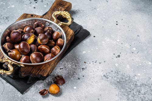 Preview: Cracked roasted chestnuts served in a skillet. Gray background. Top view. Copy space