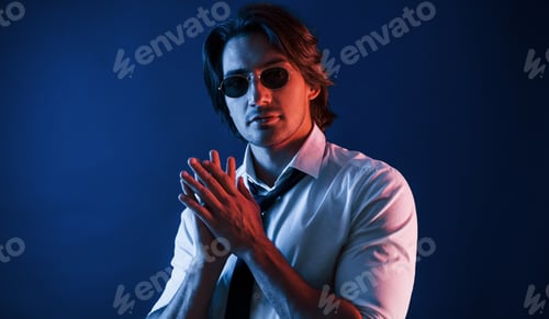 Preview: Beautiful man in formal wear and in glasses is in the studio with blue neon lighting