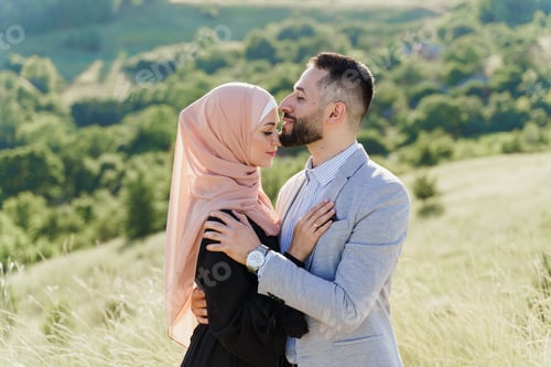 Preview: Muslim love story: couple hugs on green hills, woman in hijab smiles at her man. Dating ad.