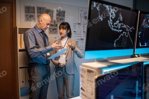 Preview: Two colleagues discussing paper while standing by whiteboard with business documents