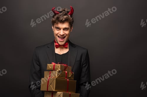 Preview: cheerful man in devil costume on halloween holding presents on black