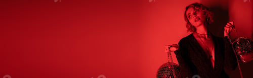 Preview: young woman with blonde hair standing in black dress and holding chains with disco balls on red,