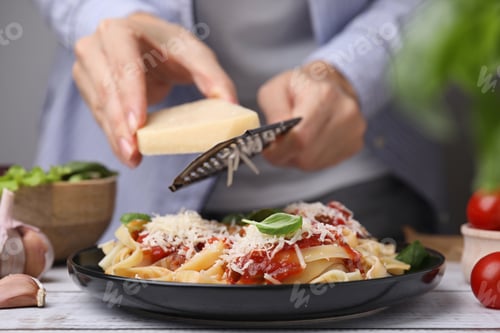 Preview: Woman grating parmesan cheese onto delicious pasta at wooden table, closeup