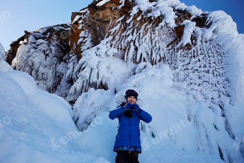 Preview: A joyful girl stands by the snowy rock.