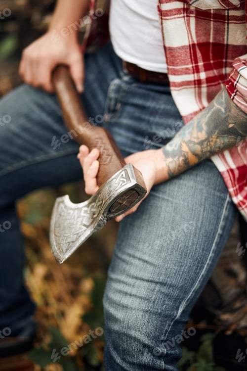 Preview: close up man in checkered shirt sitting on logs and holding axe