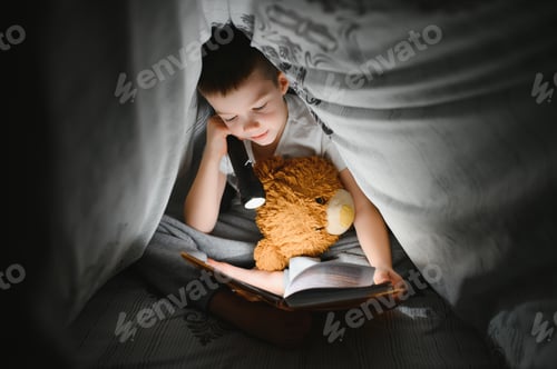 Preview: Reading book and using flashlight. Young boy in casual clothes lying down near tent at evening time