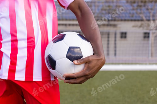 Preview: An African American young male athlete in striped red and white soccer uniform holding a soccer ball