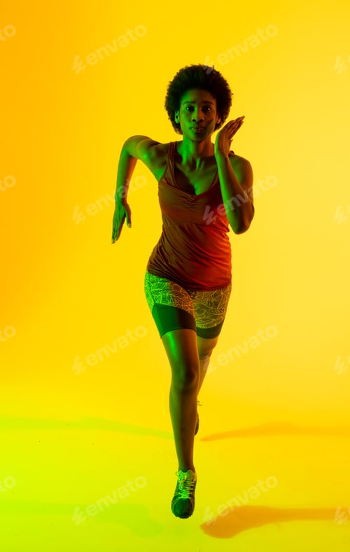 Preview: Vertical image of african american female athlete running in yellow lighting