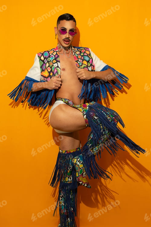 Preview: Portrait of beautiful fashionable drag queen in multicolored costume with yellow background.
