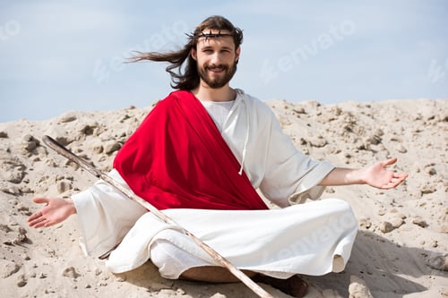 Preview: smiling Jesus in robe, red sash and crown of thorns sitting in lotus position with open arms on sand