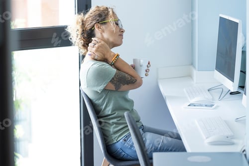 Preview: Tired woman worker sitting at the desk massaging neck and shoulders for overwork
