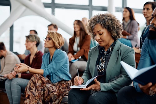 Preview: Mature businesswoman taking notes while participating in an education event at convention center.