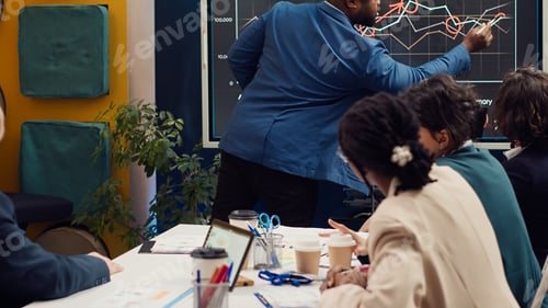 Preview: Diverse colleagues reviewing monthly sales infographics on interactive board