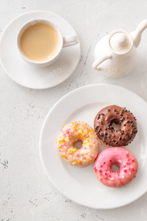 Preview: Trio of glazed donuts with coffee cup and pitcher in bright morning light