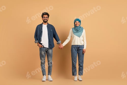 Preview: Romantic Young Muslim Couple Holding Hands While Standing Together Over Beige Background