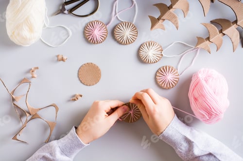 Preview: Children's hands wrap yarn on a cardboard circle for DIY Christmas handmade decorations. Top view.