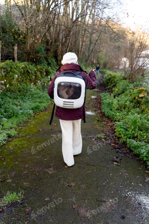 Preview: Woman walking with cat in backpack on hiking trail