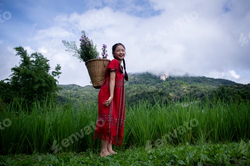 Preview: young girl dressed in traditional clothing, carrying a basket filled with flowers on her back. She i