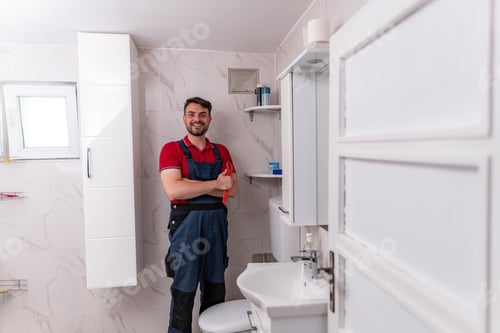 Preview: Plumber in modern bathroom smiling and posing with tools after completing repairs