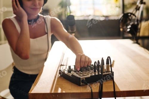 Preview: Hand of young woman rotating mixer console on soundboard by workplace