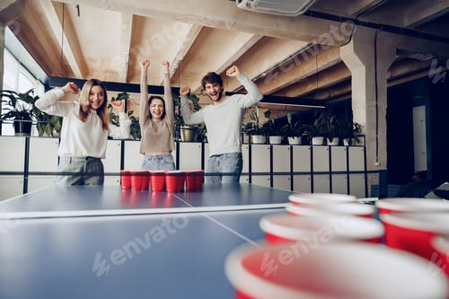 Preview: Young people coworkers playing beer pong in modern office
