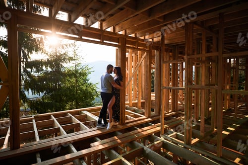 Preview: Man and woman inspecting their future wooden frame house nestled in the mountains near forest.