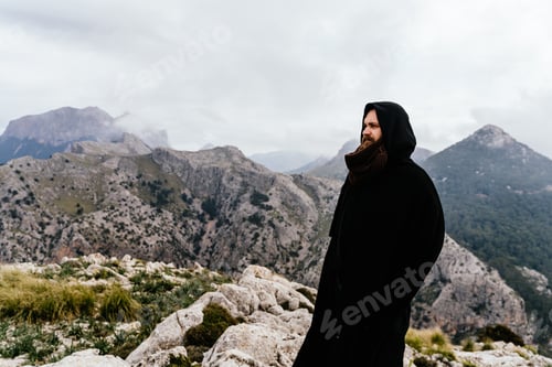 Preview: Caucasian man with long hair and beard wearing a cape standing on the mountain