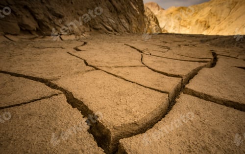 Preview: Closeup of ground fissure in a desert with rocky hills and sunlight in the background
