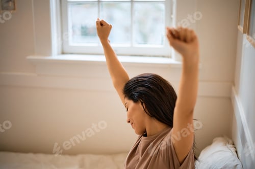 Preview: Smiling woman stretching while waking up in her bedroom.