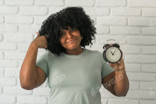 Preview: Surprised african american woman holding alarm clock amazed with open mouth and surprise happy face