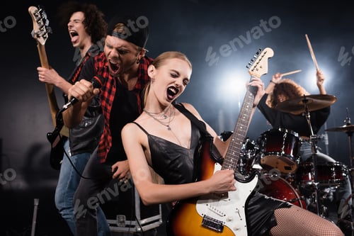 Preview: KYIV, UKRAINE - AUGUST 25, 2020: Blonde woman playing electric guitar while shouting with vocalist