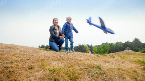 Vista previa: Happy excited little boy with mother throwing toy airplane from the hill at park