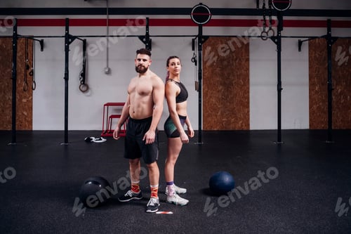 Preview: Young woman and man training together, back to back portrait in gym