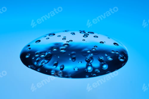 Preview: The viscous gel serum for the face flows and collects into a drop on a blue background..