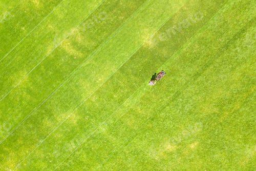 Preview: Aerial view of small figure of man worker trimming green grass with mowing mashine