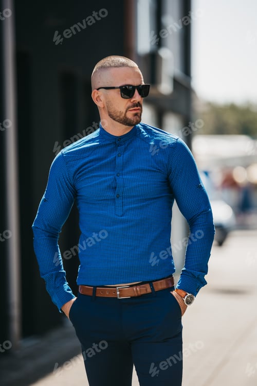 Preview: Cool handsome Caucasian man wearing a blue shirt and sunglasses posing outdoor