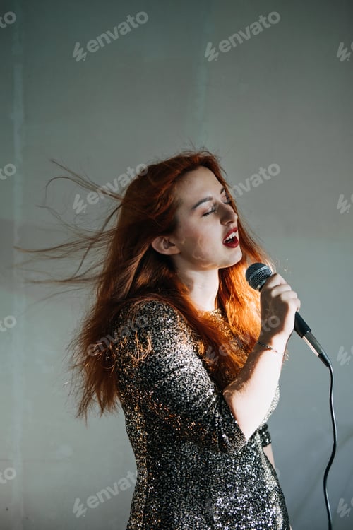Preview: Portrait of redhead female singer woman in sparkly evening dress holding microphone