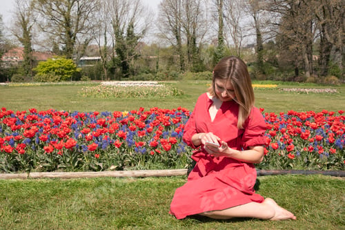 Preview: A young beautiful girl in a red dress in the park waved her hair, with spring tulips writes sms