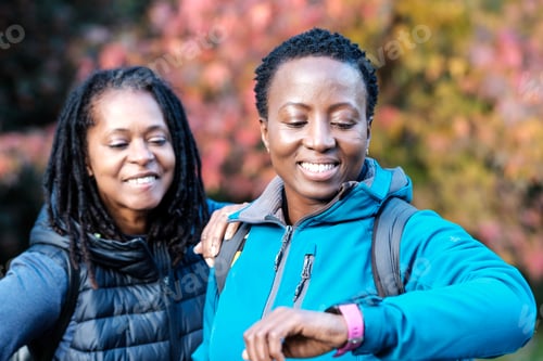 Preview: Portrait of two black mature women checking smart watch outdoors.