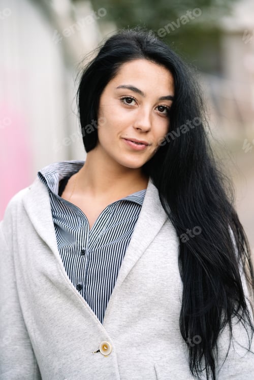 Preview: Young Caucasian woman with long black hair posing in the street in urban